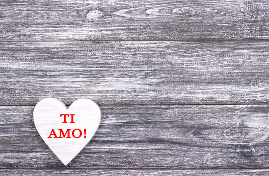 Decorative white wooden heart on grey wooden background with lettering I Love You in Italian.