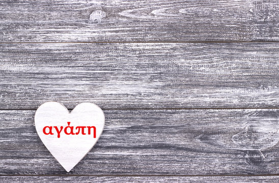 Decorative white wooden heart on grey wooden background with lettering Love in Greek.