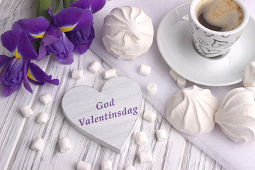 Still life with cup of coffe marshmallow zephyr iris flowers heart sign with lettering Happy Valentines Day in Norwegian on white wooden background. Love