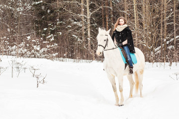 Fototapeta na wymiar Nice girl and white horse outdoor in snowfall in a winter