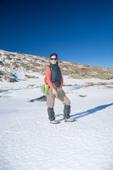 brunette sport active woman with green vest, red sweater, brown trousers walking hiking in snow with blue sky in Gredos mountain, Avila, Spain, Europe
