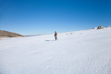 brunette sport active woman with green vest, red sweater, brown trousers walking hiking in snow with blue sky in Gredos mountain, Avila, Spain, Europe
