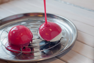 Two sphere cakes lay on metal tray on white wooden table. Enrobing process