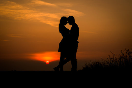 silhouette teenager lovers couple with sun between on sunset dusk sky background: black shadow hand drawn of people hug and kiss people:passion in love concept:decoration,design,valentines