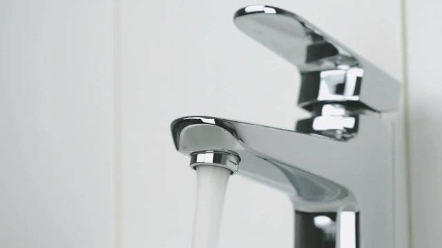 Stylish faucet in bathroom. The flow of water is pouring from chrome-plated faucet. Close-up