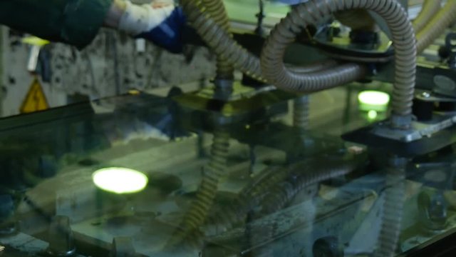 Some Rubber Robot Crane Takes a Triplex Glass Pane and Puts in a Vertical Pack, Being Accompanied by a Worker in a Green Uniform