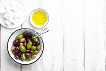 Fresh olives, feta cheese and olive oil on white wooden background