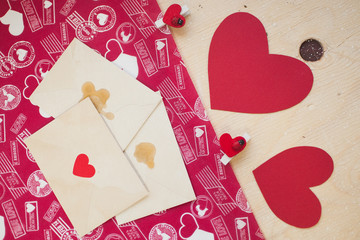 Red paper hearts with pins and envelopes on a wood table