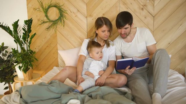 loving family of three lying on bed in morning. Family hugging and reading book