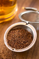 Rooibos herbal tea in strainer with freshly prepared tea in the back, photographed with natural light (Selective Focus, Focus one third into the leaves)