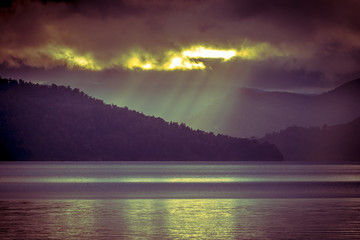 Sunrays falling through clouds over foggy mountain lake in vinta
