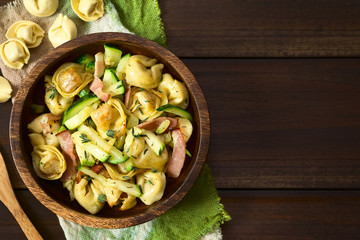 Baked cheese tortellini or belly button pasta with zucchini, bacon and thyme in wooden bowl, photographed overhead on dark wood with natural light (Selective Focus, Focus on the top of the dish) - obrazy, fototapety, plakaty