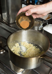 Turmeric powder being dropped into a pan of frying  minced garlic and finely sliced onion. Step by step recipe cooking.