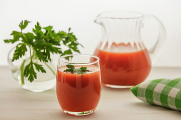 The juice from the tomatoes on a light background. Tomato juice in pitcher and in the glass. Vegetable juice. Of parsley in the glass. Green napkin on the table. Studio light.
