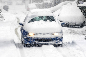 A snow covered car drives in winter storm