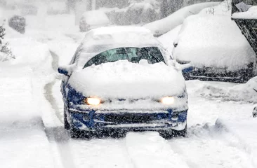 Papier Peint photo Orage Une voiture couverte de neige conduit dans une tempête hivernale