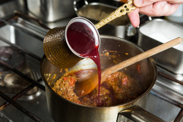 Sweet blended pomegranate sauce being poured into a hot frying pan of ingredients - obrazy, fototapety, plakaty