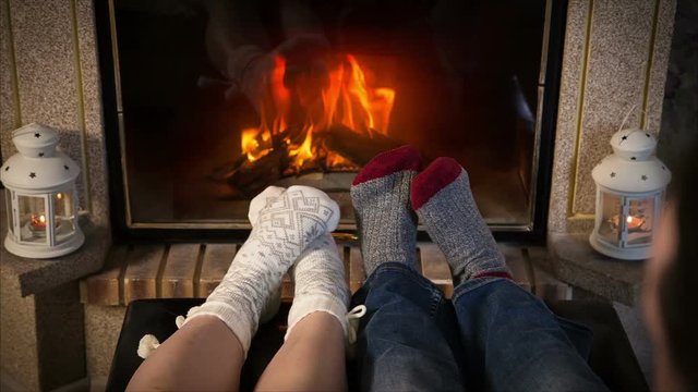Legs of couple in woolen socks heat up near fireplace