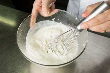 A beautiful rich and creamy , white whipped cream mixture, being hand whisked in a large glass mixing bowl.
