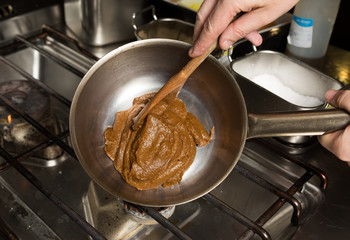 Rich thick brown curry paste being mixed and cooked in a metal frying pan, over a metal kitchen hob.