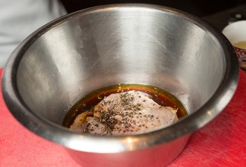 An organic, free range raw duck fillet, being marinated in a metal mixing bowl.