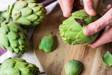 Man's hand holding knife and peeling fresh artichokes, preparing