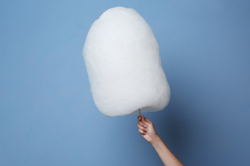 Female hand holding cotton candy on blue background