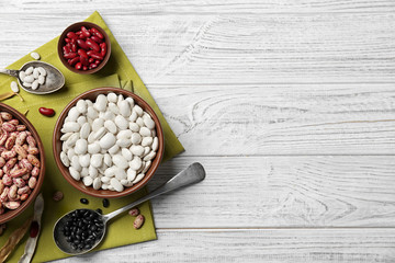 Assortment of haricot beans in bowls and spoons on white wooden background