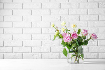 Glass vase with bouquet of beautiful flowers on brick wall background
