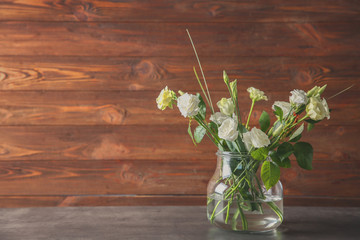 Glass vase with bouquet of beautiful roses on wooden background