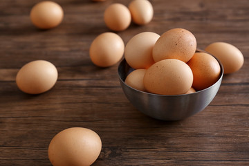 Raw eggs in bowl on wooden background