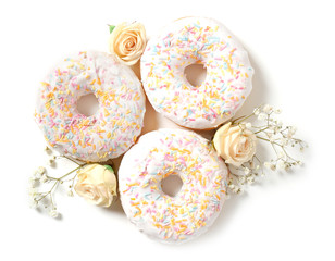 Delicious doughnuts and beautiful flowers on white background