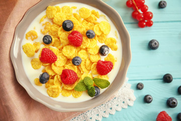 Tasty cornflakes with raspberries and blueberries on blue background