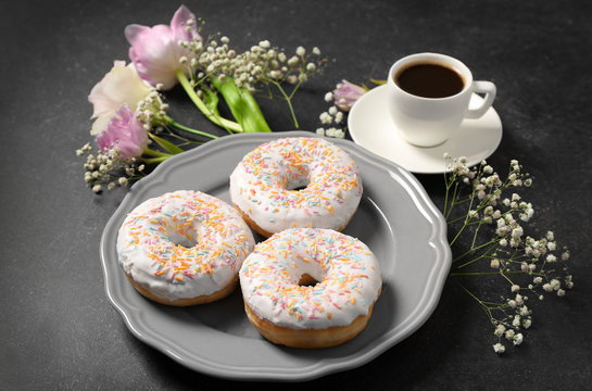 Plate with delicious doughnuts, cup of coffee and beautiful flowers on grey background