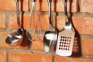 Set of metal kitchen utensils hanging on brick wall