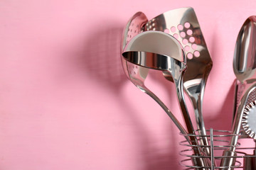 Kitchen utensils in holder on color background