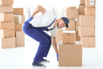 Man suffering from back ache while moving boxes indoors