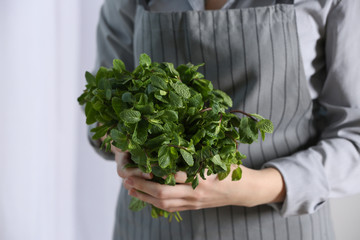 Woman in apron holding bunch of fresh mint, closeup