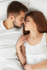 Cute young couple lying in bed at home