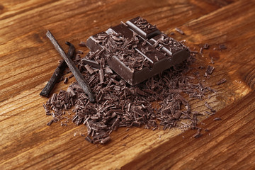 Broken chocolate pieces and shavings on wooden background