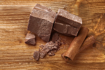 Broken chocolate pieces with cinnamon sticks on wooden background