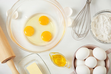 Cracked eggs in a glass bowl and ingredients for a pie on kitchen table