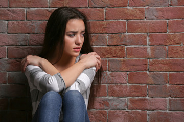 Depressed young woman on brick wall background