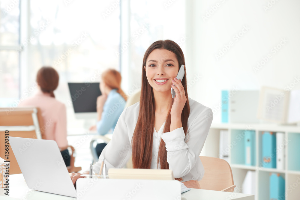 Canvas Prints Beautiful young woman talking by mobile phone while working in office