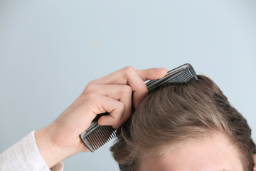 Handsome young man combing hair on color background, closeup