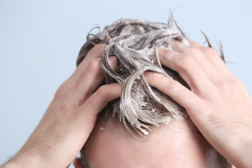Young man washing hair on color background, closeup