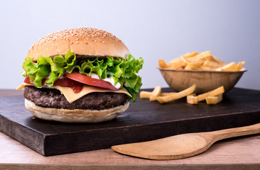 beef burger with salad and tomato on top of a wooden board and white background
