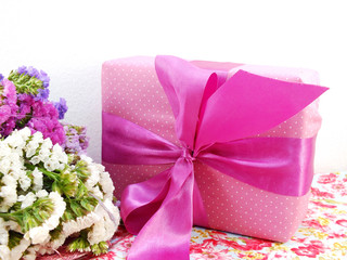 pink gift box with ribbon and flower bouquet on printed fabric background