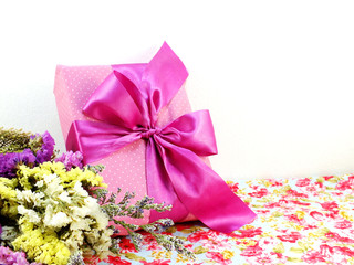 pink gift box with ribbon and flower bouquet on printed fabric background