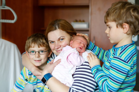 Mother holding newborn baby girl on arm with two kids boys